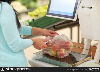 shopping, sale, consumerism and people concept - woman weighing apples on scale at grocery store. woman weighing apples on scale at grocery store