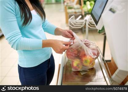 shopping, sale, consumerism and people concept - woman weighing apples on scale at grocery store. woman weighing apples on scale at grocery store