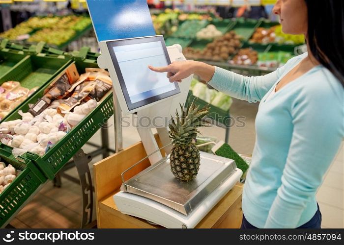 shopping, sale, consumerism and people concept - woman weighing pineapple on scale at grocery store
