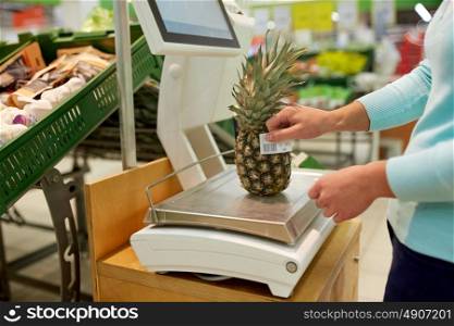 shopping, sale, consumerism and people concept - woman weighing pineapple on scale at grocery store. woman weighing pineapple on scale at grocery store