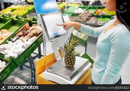 shopping, sale, consumerism and people concept - woman weighing pineapple on scale at grocery store. woman weighing pineapple on scale at grocery store. woman weighing pineapple on scale at grocery store