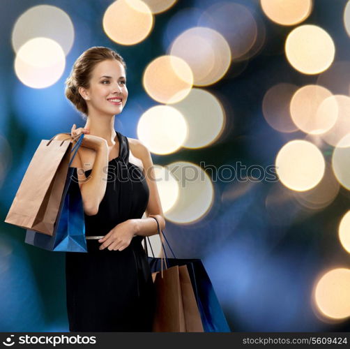 shopping, sale, gifts and holidays concept - smiling woman in dress with shopping bags over black background