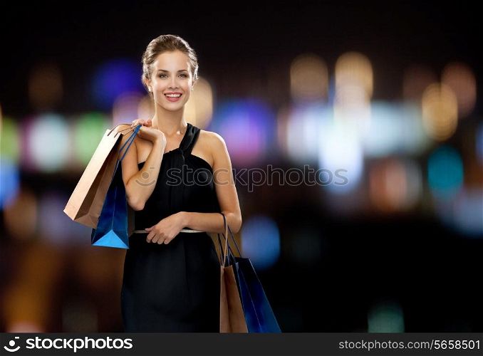 shopping, sale, gifts and holidays concept - smiling woman in dress with shopping bags over black background