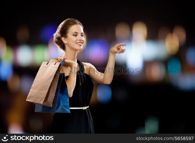 shopping, sale, gifts and holidays concept - smiling woman in dress with shopping bags over black background