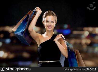 shopping, sale, gifts and holidays concept - smiling woman in dress with shopping bags over black background