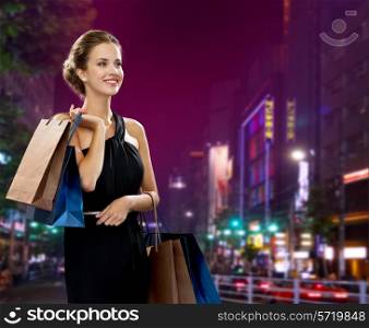 shopping, sale, gifts and holidays concept - smiling woman in evening dress with shopping bags over night city background