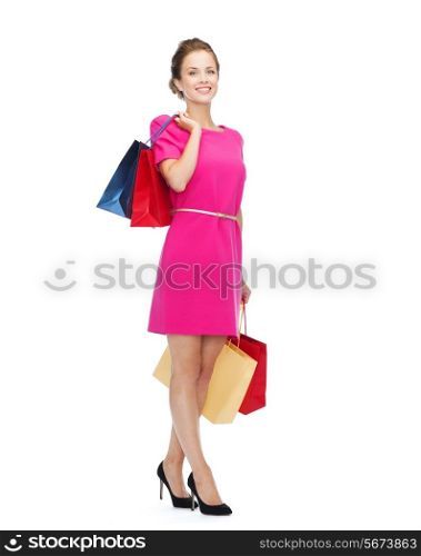 shopping, sale, gifts and holidays concept - smiling woman in pink dress with shopping bags