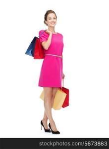 shopping, sale, gifts and holidays concept - smiling woman in pink dress with shopping bags