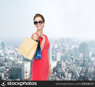 shopping, sale, gifts and holidays concept - smiling woman in red dress and sunglasses with shopping bags