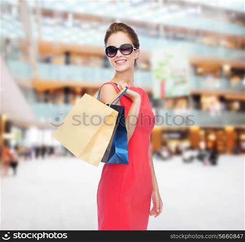 shopping, sale, gifts and holidays concept - smiling woman in red dress and sunglasses with shopping bags