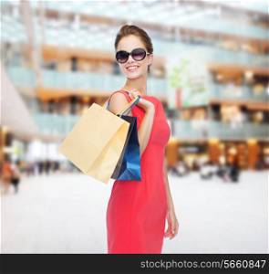 shopping, sale, gifts and holidays concept - smiling woman in red dress and sunglasses with shopping bags