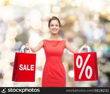 shopping, sale, gifts, christmas and holiday concept - smiling young woman in red dress with shopping bags with percent and sale sign