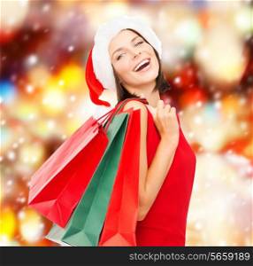 shopping, sale, gifts, christmas concept - smiling woman in red dress and santa helper hat with shopping bags