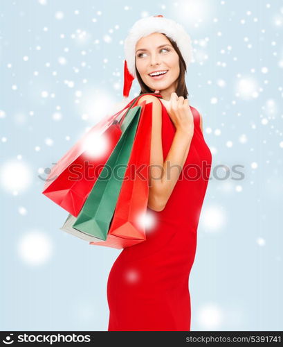 shopping, sale, gifts, christmas, x-mas concept - smiling woman in red dress and santa helper hat with shopping bags