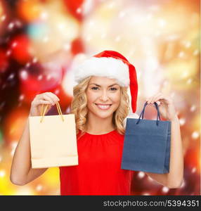 shopping, sale, gifts, christmas, x-mas concept - smiling woman in red dress and santa helper hat with shopping bags