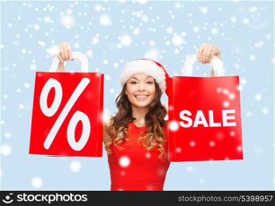 shopping, sale, gifts, christmas, x-mas concept - smiling woman in red dress and santa helper hat with shopping bags