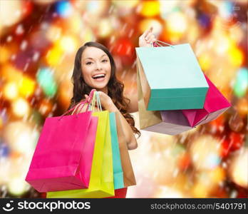 shopping, sale, gifts, christmas, x-mas concept - smiling woman in red dress with colorful shopping bags