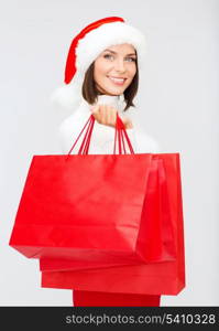 shopping, sale, gifts, christmas, x-mas concept - smiling woman in santa helper hat with shopping bags