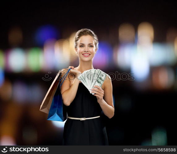 shopping, sale, gifts, money and holidays concept - smiling woman in dress with shopping bags and money over black background