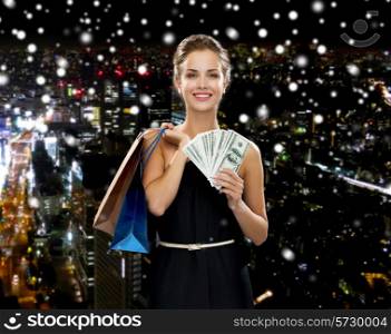 shopping, sale, gifts, money and holidays concept - smiling woman in dress with shopping bags and money over snowy night city background