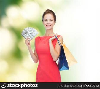 shopping, sale, gifts, money and holidays concept - smiling woman in red dress with shopping bags and money
