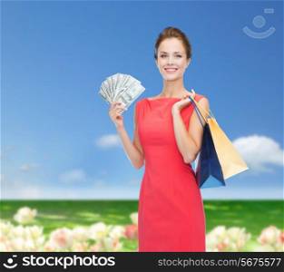 shopping, sale, gifts, money and holidays concept - smiling woman in red dress with shopping bags and money