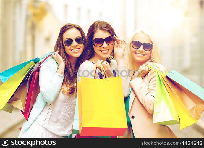 shopping, sale, happy people and tourism concept - three beautiful girls in sunglasses with shopping bags in ctiy