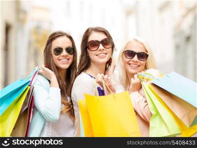 shopping, sale, happy people and tourism concept - three beautiful girls in sunglasses with shopping bags in ctiy