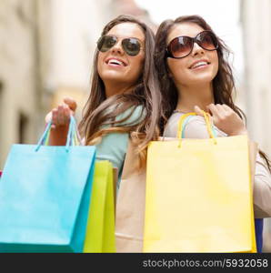 shopping, sale, happy people and tourism concept - two smiling girls in sunglasses with shopping bags in ctiy