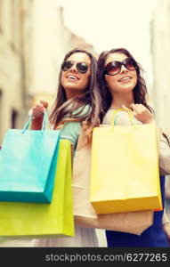 shopping, sale, happy people and tourism concept - two smiling girls in sunglasses with shopping bags in ctiy