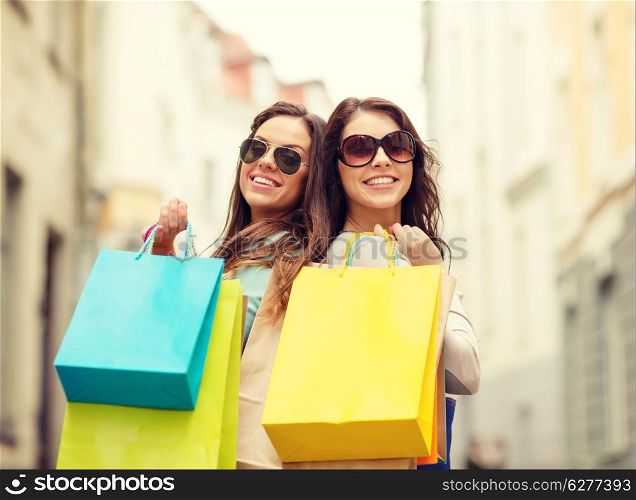 shopping, sale, happy people and tourism concept - two smiling girls in sunglasses with shopping bags in ctiy