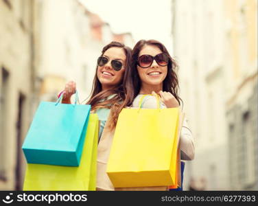 shopping, sale, happy people and tourism concept - two smiling girls in sunglasses with shopping bags in ctiy