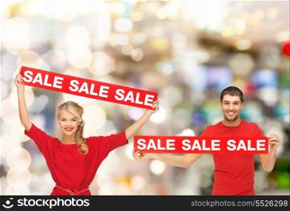 shopping, sale, mall and christmas concept - smiling woman and man with red sale signs at shopping mall