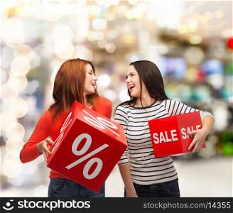 shopping, sale, mall and gift sconcept - two smiling teenage girls with percent and sale sign on red box at shopping mall