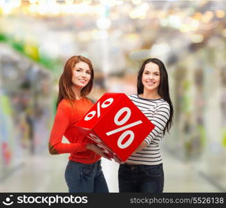 shopping, sale, mall and gift sconcept - two smiling teenage girls with percent sign on red box at shopping mall