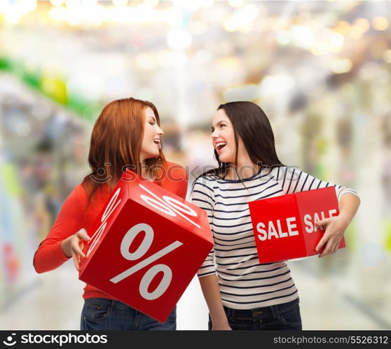 shopping, sale, mall and gift sconcept - two smiling teenage girls with percent and sale sign on red box at shopping mall