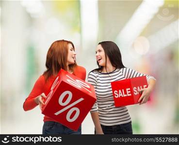shopping, sale, mall and gift sconcept - two smiling teenage girls with percent and sale sign on red box at shopping mall