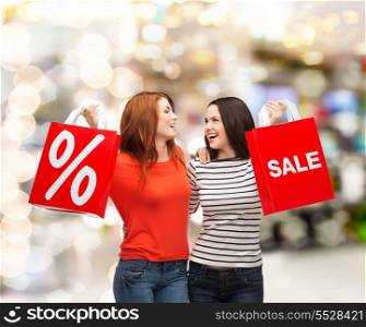 shopping, sale, mall and gift sconcept - two smiling teenage girls with shopping bags and percent sign at shopping mall