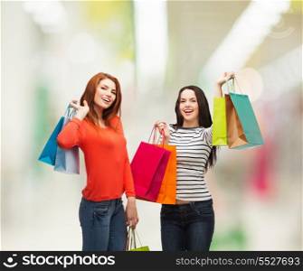 shopping, sale, mall and gifts concept - two smiling teenage girls with shopping bags at shopping mall