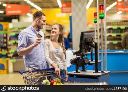 shopping, sale, payment, consumerism and people concept - happy couple with bank card buying food at grocery store or supermarket self-service cash register