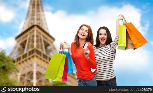 shopping, sale, tourism and people concept - two smiling teenage girls with shopping bags and credit card over paris eiffel tower background