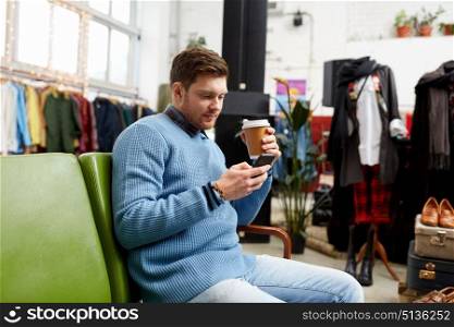 shopping, technology and people concept - man with smartphone drinking coffee at vintage clothing store. man with smartphone and coffee at clothing store. man with smartphone and coffee at clothing store