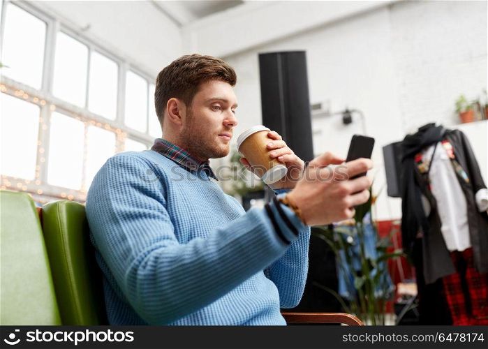 shopping, technology and people concept - man with smartphone drinking coffee at vintage clothing store. man with smartphone and coffee at clothing store. man with smartphone and coffee at clothing store