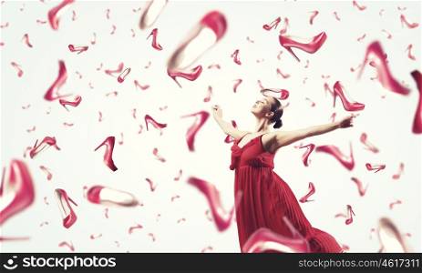 Shopping therapy. Young cheerful woman in dress and many falling shoes