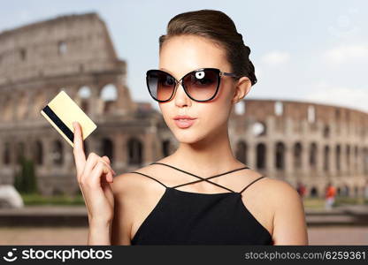 shopping tour, finances, travel, people and luxury concept - beautiful young woman in elegant black sunglasses with credit card over coliseum background