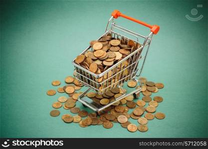 Shopping trolley with coins on a green background