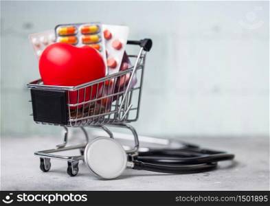 Shopping trolley with medicines for online purchase with red heart and stethoscope on light.