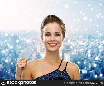 shopping, wealth, christmas, holidays and people concept - smiling woman in evening dress holding credit card over snowy city background