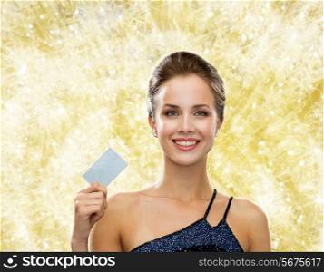 shopping, wealth, christmas, holidays and people concept - smiling woman in evening dress holding credit card over yellow lights background
