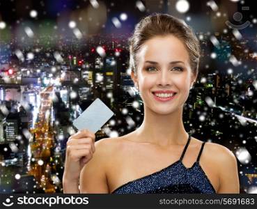 shopping, wealth, christmas, holidays and people concept - smiling woman in evening dress holding credit card over snowy night city background